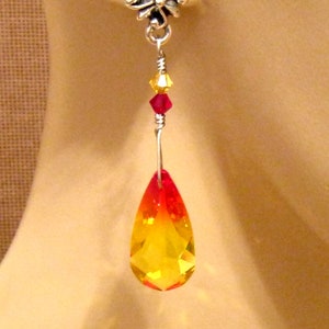 May include: A single earring with a silver-colored floral stud. A wire descends, holding yellow and red crystals, leading to a large, teardrop-shaped crystal that transitions from red to yellow. The earring is designed to dangle.