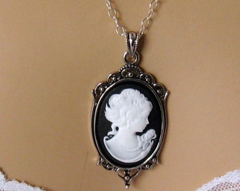 Op de afbeelding: Een zilveren ketting met een zwart-witte cameo hanger. De cameo toont het profiel van een vrouw in wit tegen een zwarte achtergrond.