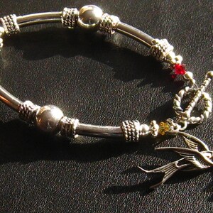 May include: A silver bracelet with a silver bird charm, red and yellow beads, and a silver toggle clasp.