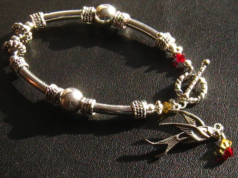 May include: A silver bracelet with a silver bird charm, red and yellow beads, and a silver toggle clasp.