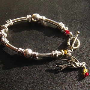 May include: A silver bracelet with a bird charm, red and gold beads, and a toggle clasp.