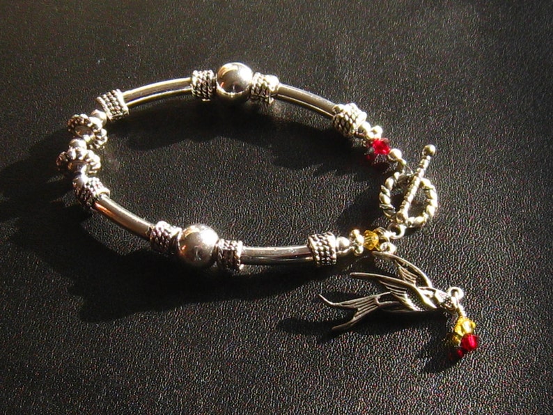 May include: A silver bracelet with a bird charm, red and gold beads, and a toggle clasp.