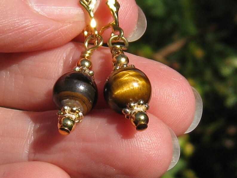 May include: Gold earrings with tiger's eye beads. The beads are round and have a brown and gold colour.