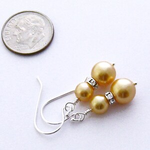 May include: A pair of gold pearl earrings with silver hooks and clear rhinestone accents.