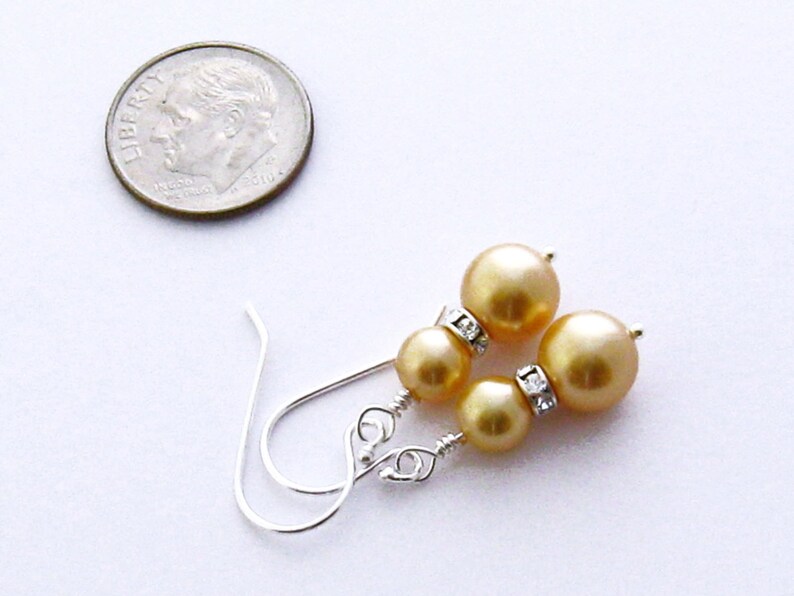 May include: A pair of gold pearl earrings with silver hooks and clear rhinestone accents.