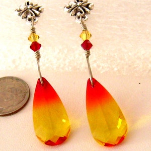 May include: A pair of dangle earrings featuring teardrop-shaped, faceted crystals that transition from red to yellow. The earrings have silver-tone metal accents, including floral studs and wire detailing, with red and yellow beads.