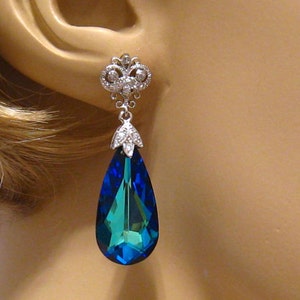 May include: Silver dangle earrings with a teardrop-shaped blue crystal and a smaller crystal cluster at the top.