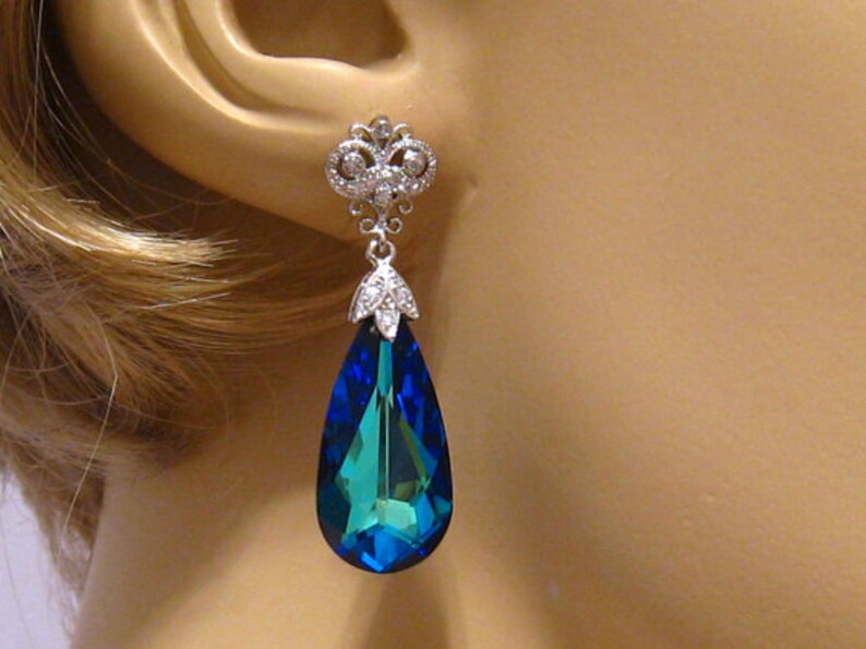 May include: Silver dangle earrings with a teardrop-shaped blue crystal and a smaller crystal cluster at the top.