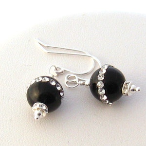 May include: Black onyx earrings with a silver hook and a row of clear rhinestones around the onyx bead.