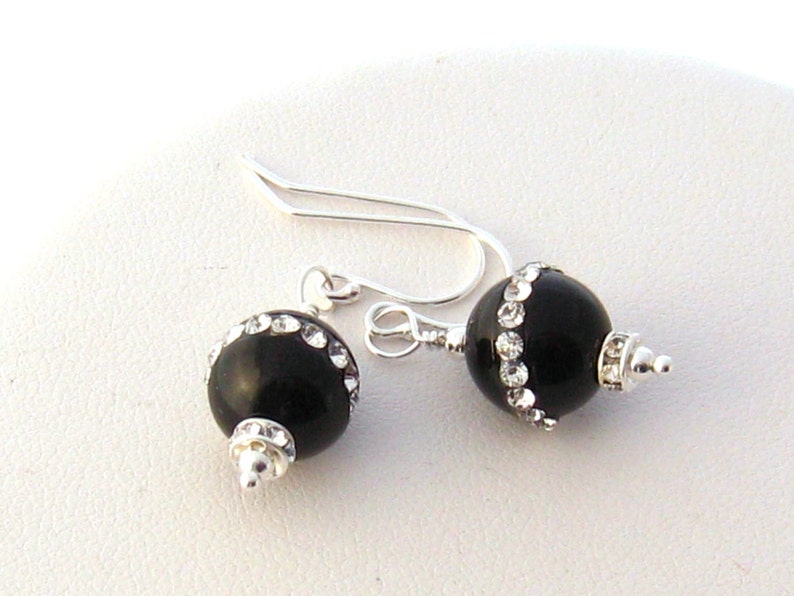 May include: Black onyx earrings with a silver hook and a row of clear rhinestones around the onyx bead.