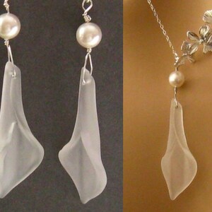 May include: A delicate necklace and earrings set featuring a clear glass pendant shaped like a flower with a pearl accent. The necklace has a silver chain and a floral design.