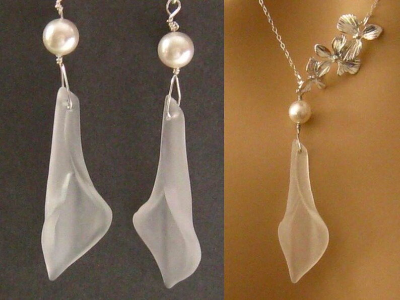 May include: A delicate necklace and earrings set featuring a clear glass pendant shaped like a flower with a pearl accent. The necklace has a silver chain and a floral design.