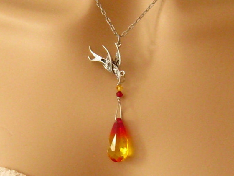 May include: A silver necklace with a bird pendant and a teardrop-shaped crystal that is red and yellow.