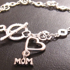 May include: Silver bracelet with a heart charm and a charm that says "MOM". The bracelet has a toggle clasp.