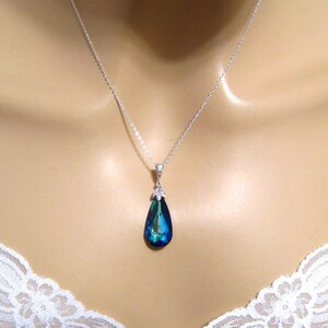 May include: A silver chain necklace with a teardrop-shaped pendant. The pendant is a deep blue color with a green hue.