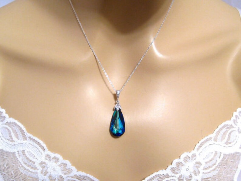 May include: A silver chain necklace with a teardrop-shaped pendant. The pendant is a deep blue color with a green hue.
