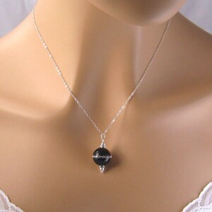 May include: A silver chain necklace with a black round pendant. The pendant is set in a silver frame with small decorative accents.