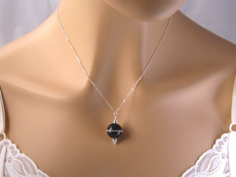 May include: A silver chain necklace with a black round pendant. The pendant is set in a silver frame with small decorative accents.
