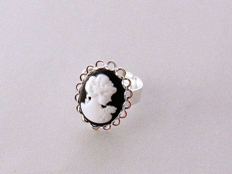 May include: A silver ring with a black cameo featuring a white silhouette of a woman's profile.