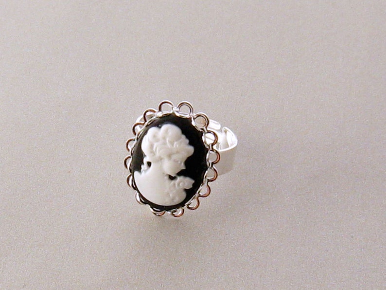 May include: A silver ring with a black cameo featuring a white silhouette of a woman's head.