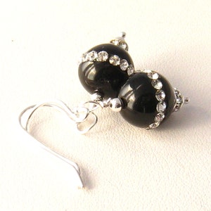 May include: Black dangle earrings with a silver hook and two black beads accented with clear rhinestones.