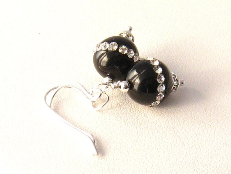 May include: Black dangle earrings with a silver hook and two black beads accented with clear rhinestones.