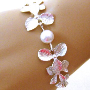 May include: A silver bracelet with a pearl charm and orchid flower designs.