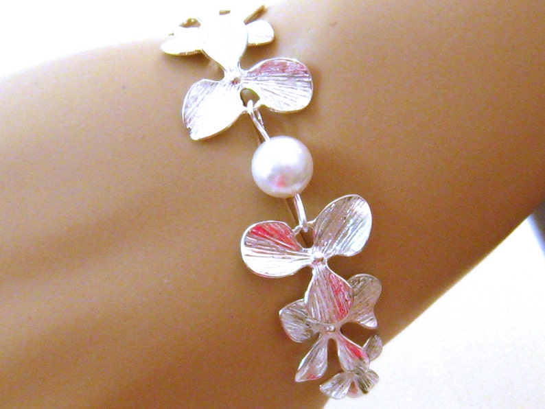 May include: A silver bracelet with a pearl charm and orchid flower designs.