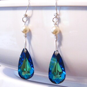 May include: A pair of dangle earrings with a teardrop-shaped blue and green crystal and a white pearl accent.