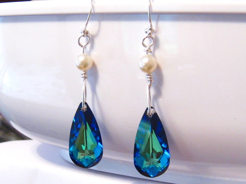 May include: A pair of dangle earrings with a teardrop-shaped blue and green crystal and a white pearl accent.