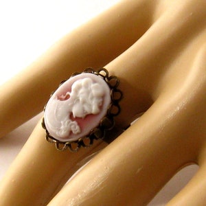 May include: A white cameo ring with a delicate gold filigree setting. The cameo features a woman's profile in relief.