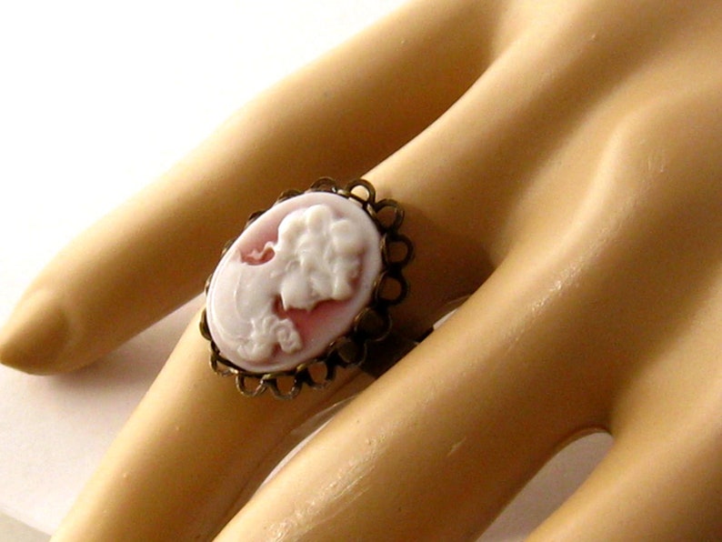 May include: A white cameo ring with a delicate gold filigree setting. The cameo features a woman's profile in relief.