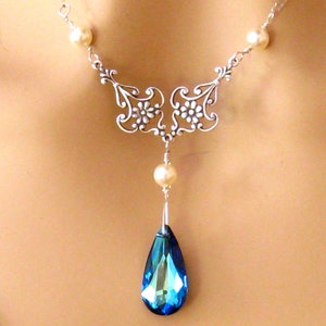 May include: A silver necklace with a teardrop-shaped blue crystal pendant and pearl accents.