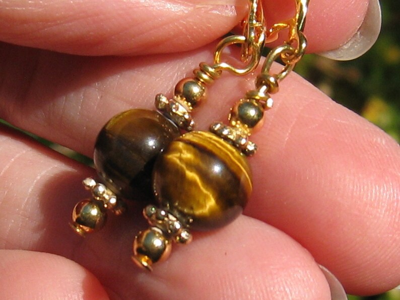 May include: Gold earrings with tiger's eye beads. The beads are round and have a brown and gold colour.