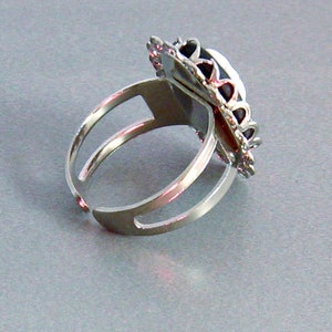 May include: A silver adjustable ring with a black and silver ornate design. The ring has a large oval-shaped setting.