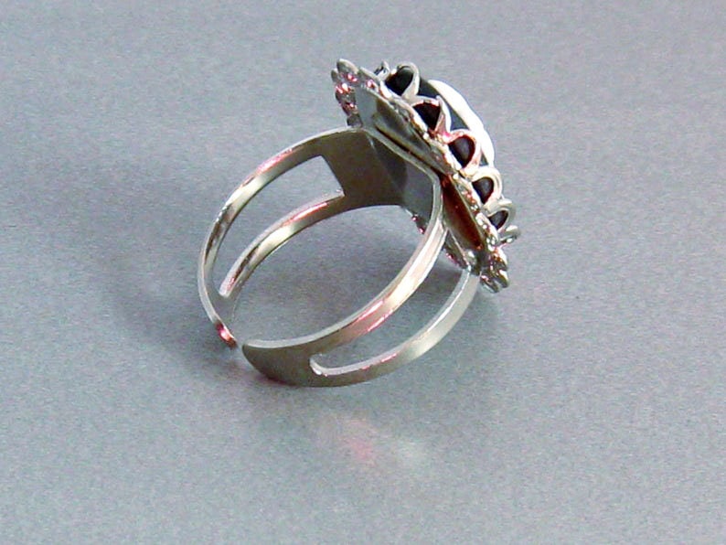 May include: A silver adjustable ring with a black and silver ornate design. The ring has a large oval-shaped setting.