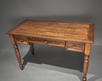 May include: A wooden desk with a rectangular top and three drawers. The desk is made of a light brown wood and has turned legs. The drawer pulls are a brass color. The desk is a classic design.