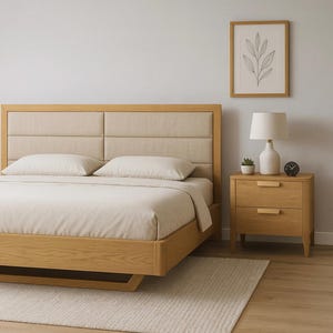 Könnte beinhalten: Ein modernes Holzbett mit einem beige gepolsterten Kopfteil und passender Bettwäsche. Ein Nachttisch aus Holz mit zwei Schubladen, eine Lampe und ein gerahmter botanischer Druck vervollständigen das Schlafzimmer-Set. Das Bett ist etwa 200 cm lang.