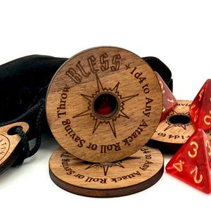 May include: A collection of wooden gaming accessories, including dice, tokens, and a black drawstring bag. The wooden tokens have engraved text and a compass design. Red, translucent, four-sided dice are also present. The text on the tokens reads "BLESS" and "ORDER".