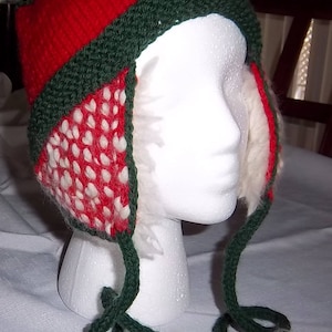 Puede incluir: Un gorro de punto rojo, verde y blanco con un pompón en la parte superior y lazos largos. El gorro tiene un forro blanco peludo.