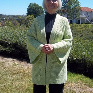 May include: A light green knitted cardigan with a long, open front and wide sleeves. The cardigan is made of a soft, textured yarn and has a relaxed fit.