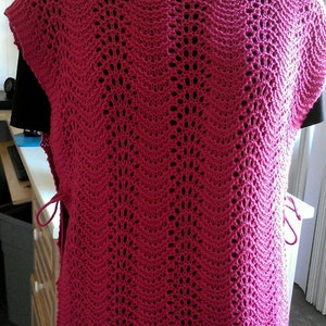 May include: A pink crocheted sleeveless top with a scalloped hem and a delicate openwork pattern.
