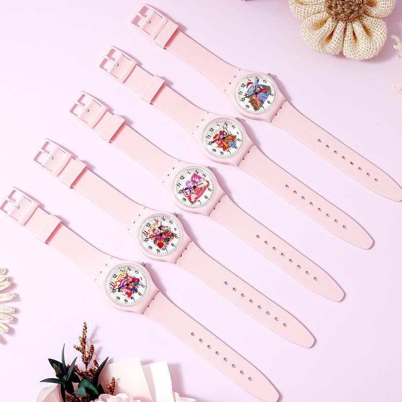 May include: Five light pink analog wristwatches with matching silicone straps and buckles. Each watch face features a unique, colorful graphic illustration of cartoon characters, black numerals, and thin black hands on a white background.