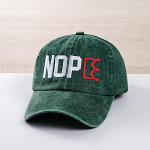 Può includere: Un cappellino da baseball verde scuro con la scritta "NOPE" ricamata in lettere bianche. La "E" è delineata in rosso. Il cappellino ha una visiera curva e un piccolo bottone sulla parte superiore.
