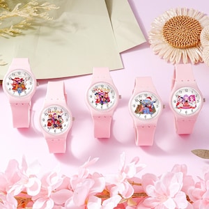 May include: Five light pink analog wristwatches with silicone bands and white faces. Each watch features a unique graphic illustration of cartoon characters and the text Huntrix. The watches have black hour, minute, and second hands with numbers.