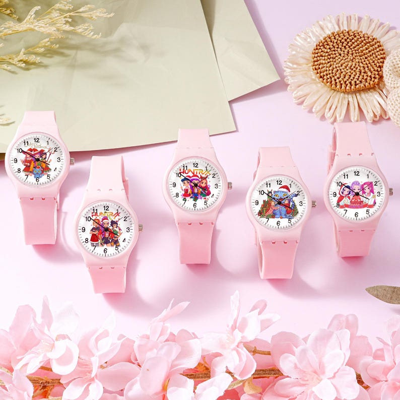 May include: Five light pink analog wristwatches with silicone bands and white faces. Each watch features a unique graphic illustration of cartoon characters and the text Huntrix. The watches have black hour, minute, and second hands with numbers.