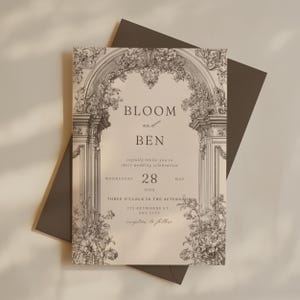 Op de afbeelding: Een trouwkaart met een bloemenboogontwerp. De uitnodiging bevat de namen "BLOOM en BEN" en de datum "28 MEI 2030". De tekst "nodigen u van harte uit voor hun huwelijksviering" is ook opgenomen. De uitnodiging staat op een lichte achtergrond met een donkergrijze envelop.