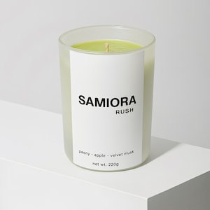 May include: A clear glass candle with a pale green wax and a wooden wick. The candle has a white label with the text "SAMIORA RUSH" and scent notes. The net weight is 220g.