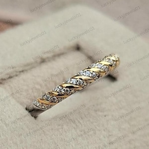 Puede incluir: Un anillo de dos tonos con un diseño trenzado que presenta bandas alternas de oro amarillo pulido y filas de pequeñas piedras blancas redondas y transparentes. La banda tiene un patrón en espiral continuo alrededor de toda la pieza.
