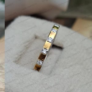 Könnte beinhalten: Ein schmaler Ring mit zweifarbigem Design, bestehend aus einem polierten Goldstreifen in der Mitte und silberfarbenen Rändern. Der Ring ist mit vier kleinen, klaren, rund geschliffenen Steinen besetzt, die gleichmäßig in einer Kanalfassung.